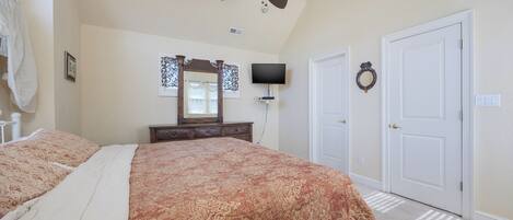 A bedroom with a large bed, a ceiling fan, a TV, and a door.