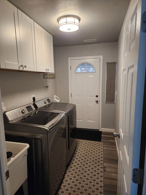 A laundry room with a front-loading washer and dryer, a white door with a window, and a patterned rug on the floor. - Lovely 2-bedroom house with AC and a Hot tub in peaceful Mormon Lake (Mormon Lake)