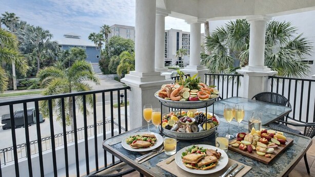 A balcony with a table set for a meal, featuring a variety of dishes and drinks.
