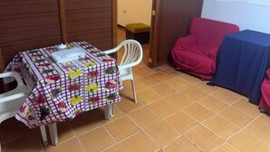 A room with a table covered by a fruit-patterned tablecloth, a white chair, a red chair, and a small stool.