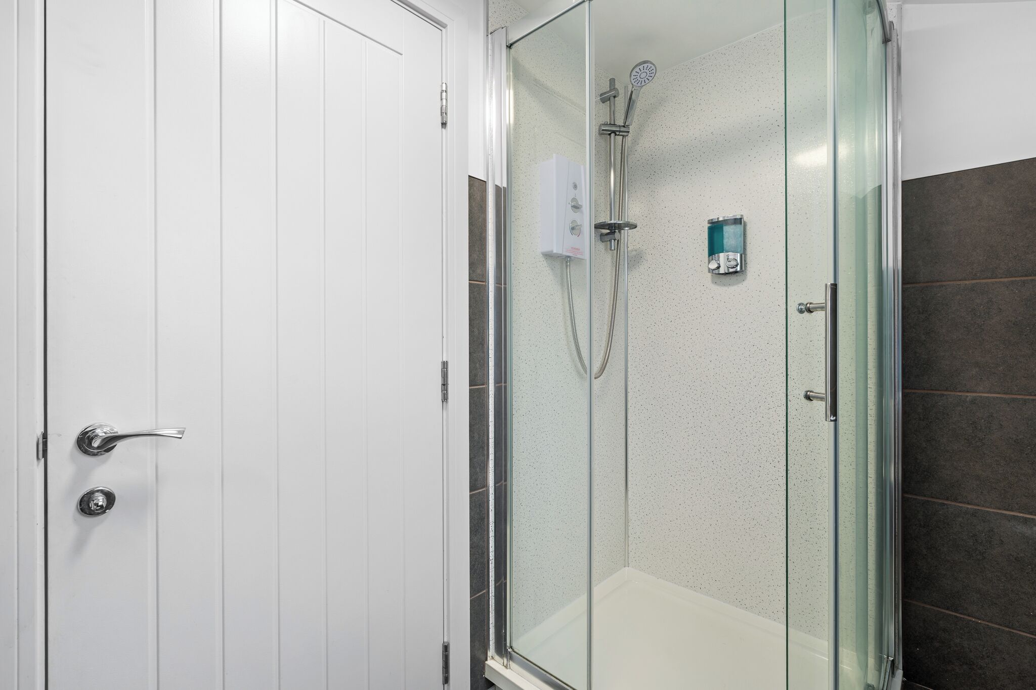 Ducha con cerramiento de vidrio, cabezal de ducha de mano y panel de control en la pared.