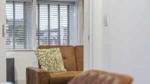 A brown armchair with a floral pillow in front of a window with blinds.