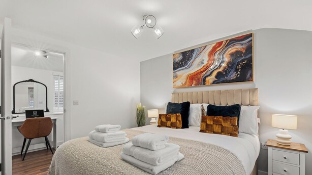 A neatly arranged bedroom with a bed, bedside tables, a desk, and a large abstract painting on the wall.