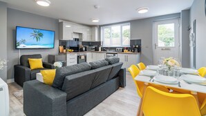 A modern kitchen with white cabinets, a dining area with yellow chairs, and a grey sofa with yellow cushions. - Fairfax Close, Amesbury, Wiltshire, SP47ST, United Kingdom (Amesbury)