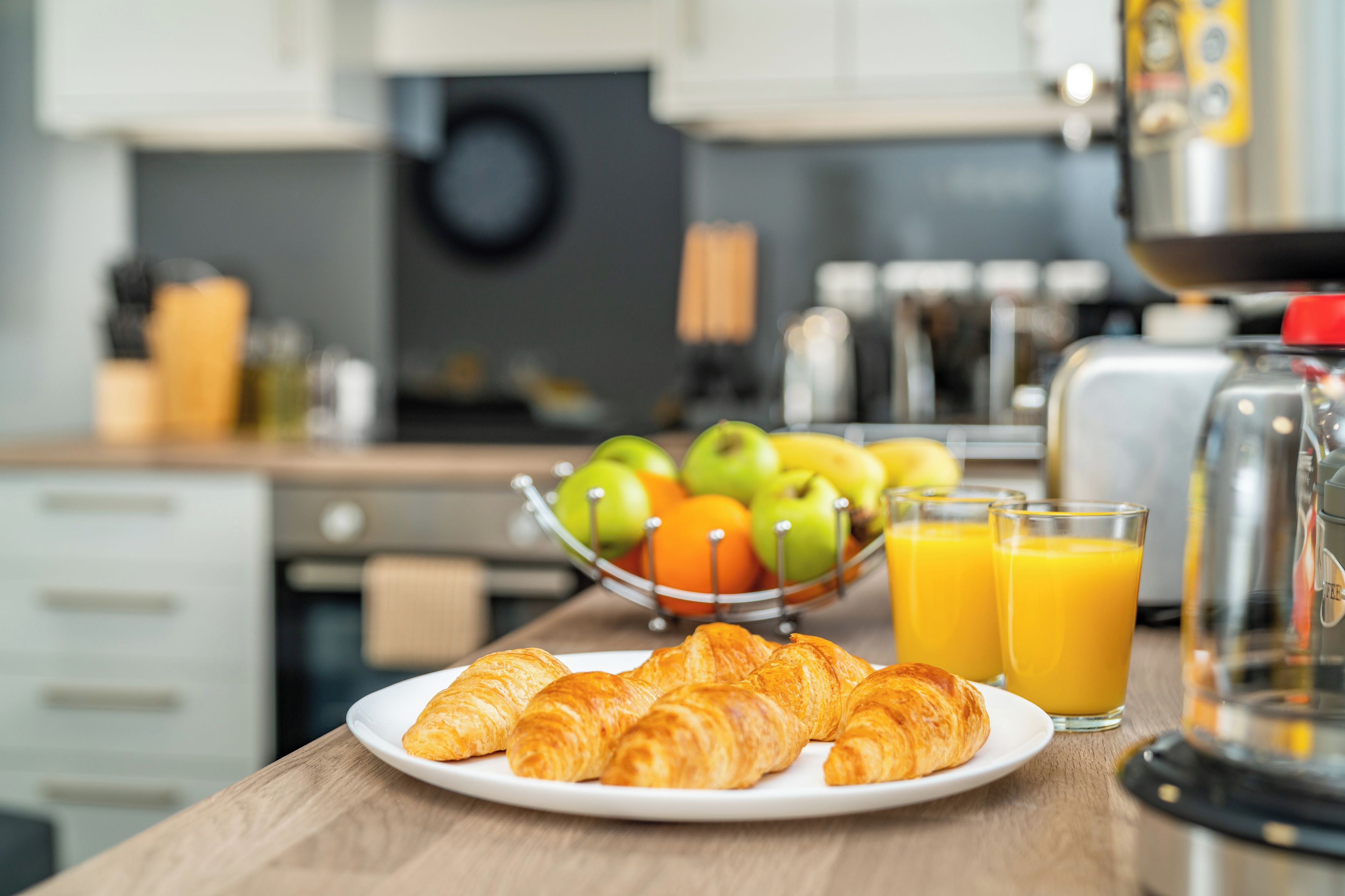 Un desayuno con cruasanes, manzanas, naranjas y zumo de naranja sobre una mesa de madera.