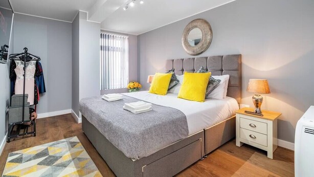 A modern bedroom with a grey bed, yellow pillows, a bedside table with a lamp, and a wardrobe with clothes. - Fairfax Close, Amesbury, Wiltshire, SP47ST, United Kingdom (Amesbury)
