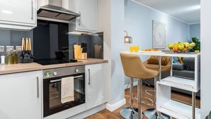 A modern kitchen with a built-in oven, a stainless steel range hood, and a bar stool with a fruit bowl. - Fairfax Close, Amesbury, Wiltshire, SP47ST, United Kingdom (Amesbury)