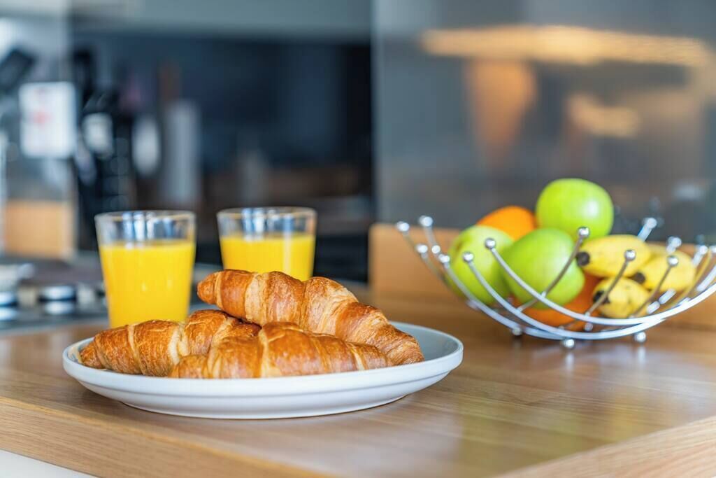 A breakfast setting with croissants on a plate, a bowl of fruit, and two glasses of orange juice.