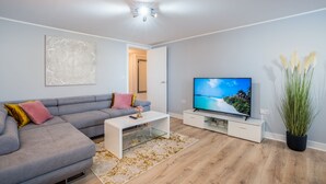 Un salon moderne avec un canapé d’angle gris, une table basse blanche, un téléviseur à écran plat et une plante en pot.