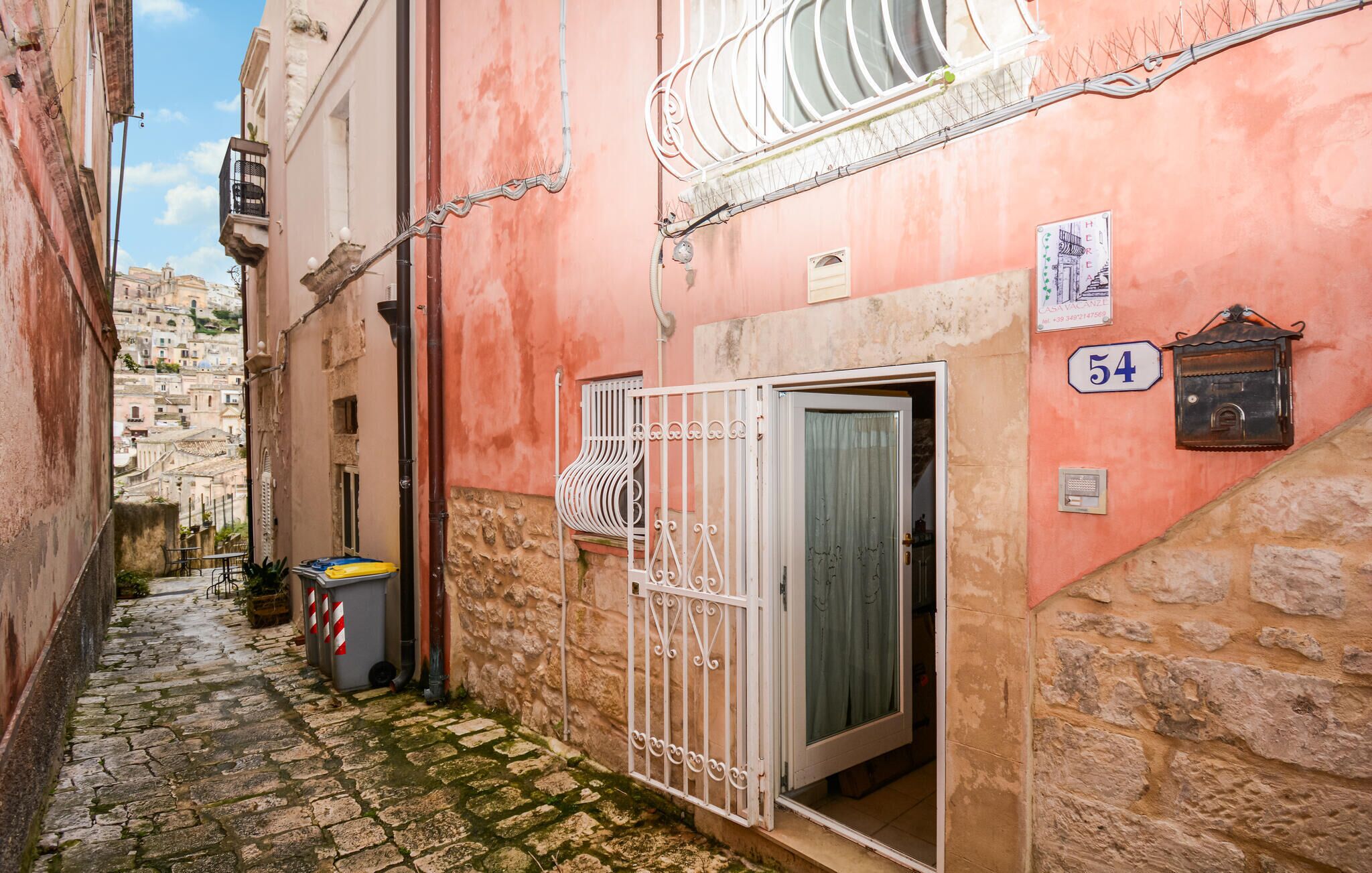 A narrow alleyway with a stone-paved path, a metal gate, and a building with a number '54' sign.