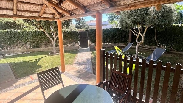 En täckt uteplats med ett bord och stolar, en pergola och utsikt över en trädgård.