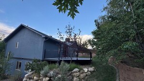 Une maison à deux étages dotée d’un balcon, entourée d’un mur de soutènement en pierre et d’une pelouse.