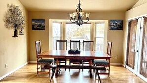 Une salle à manger spacieuse, avec une grande table en bois, six chaises, un lustre et de grandes fenêtres.