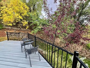 Une terrasse en bois avec deux chaises et une table, entourée d’une rambarde en métal noir.