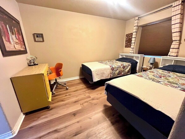 Une petite pièce bien éclairée, avec deux lits simples, un bureau avec une chaise et un petit placard.