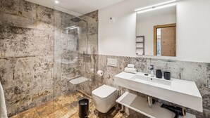 A modern bathroom with a glass shower enclosure, a white sink with a mirror above, and a marble-tiled wall. - Chalet Les Rahâs by Mrs Miggins 21 (Grimentz)