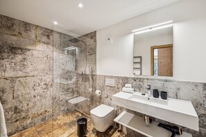 Ein modernes Badezimmer mit einer Duschkabine aus Glas, einem weißen Waschbecken mit Spiegel darüber und einer Wand mit Marmorfliesen.