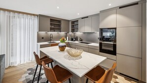 A modern kitchen with a central island, built-in appliances, and a dining area with chairs. - Chalet Les Rahâs by Mrs Miggins 21 (Grimentz)