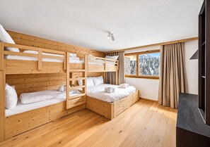 Ein Zimmer mit Etagenbetten, einem fenster mit Vorhängen und Holzdielen.
