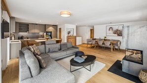 A modern living room with a sectional sofa, a dining area with a wooden table, and a kitchen with built-in cabinets. - Chalet Les Rahâs by Mrs Miggins 21 (Grimentz)