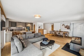Ein modernes Wohnzimmer mit einer Eckcouch, einem Essbereich mit Holztisch und einer Küche mit eingebauten Schränken.