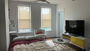 Een slaapkamer met een bed, een televisie, een bureau en twee ramen.