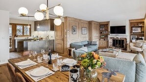 A modern kitchen with a central island, wooden cabinets, and a dining area set for six with a table, chairs, and a vase of flowers. - Starlight by Mrs Miggins (Crans-Montana)