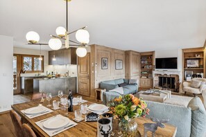 A modern kitchen with a central island, wooden cabinets, and a dining area set for six with a table, chairs, and a vase of flowers. - Starlight by Mrs Miggins (Crans-Montana)