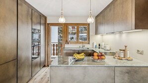A modern kitchen with wooden cabinets, a marble countertop, and hanging pendant lights. - Starlight by Mrs Miggins (Crans-Montana)