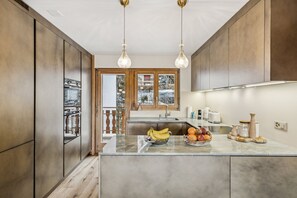 A modern kitchen with wooden cabinets, a marble countertop, and hanging pendant lights. - Starlight by Mrs Miggins (Crans-Montana)
