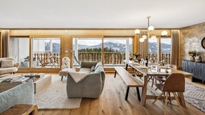 A spacious living room with a wooden floor, a large dining table, and multiple seating options. - Starlight by Mrs Miggins (Crans-Montana)
