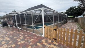 Ein überdachter Patio-Bereich mit Pool, Holzzaun und Pflasterboden.