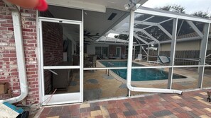A backyard with a swimming pool, enclosed patio, and a brick wall. - The Cove  Beach Pool House Walk to Beach, Dining & Shopping (Deerfield Beach)