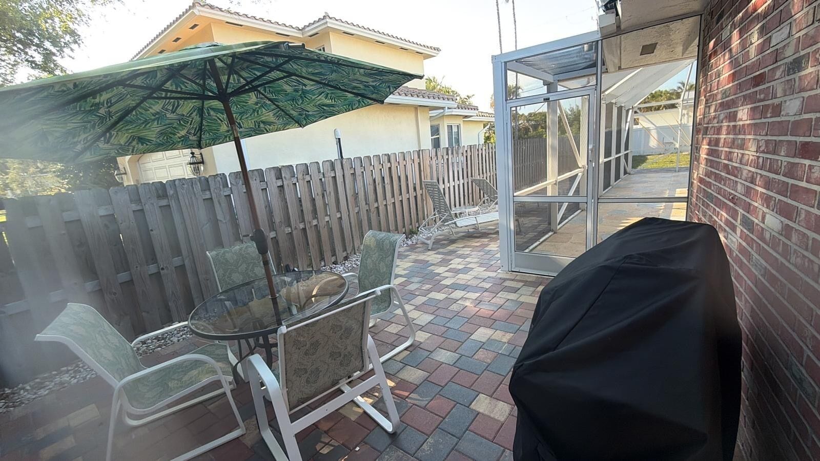 A patio with a glass table and chairs, a wooden fence, and a covered grill area.