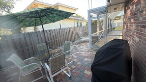 Eine Terrasse mit Glastisch und -stühlen, einem Holzzaun und einem überdachten Grillbereich.