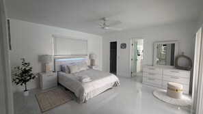 A modern bedroom with a bed, bedside tables, a dresser, a mirror, and a ceiling fan. - The Cove  Beach Pool House Walk to Beach, Dining & Shopping (Deerfield Beach)
