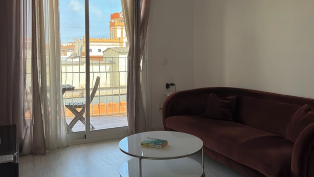 Sala de estar con un sofá rojo, una mesa de centro redonda y vistas a edificios a través de un amplio ventanal con cortinas.