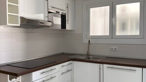 Una cocina moderna con armarios blancos, una campana extractora de acero inoxidable, horno empotrado, pileta doble y un botellero.