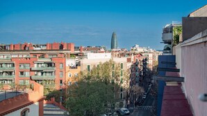Un paisaje urbano con edificios de varios pisos, una torre destacada y una calle estrecha con automóviles estacionados.