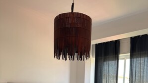 Un dormitorio con una cama grande, una lámpara colgante de madera, una ventana con cortinas y una mesita de noche.