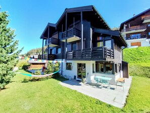 Ett hus i flera våningar med en balkong, en uteplats med utemöbler och en välskött gräsmatta.