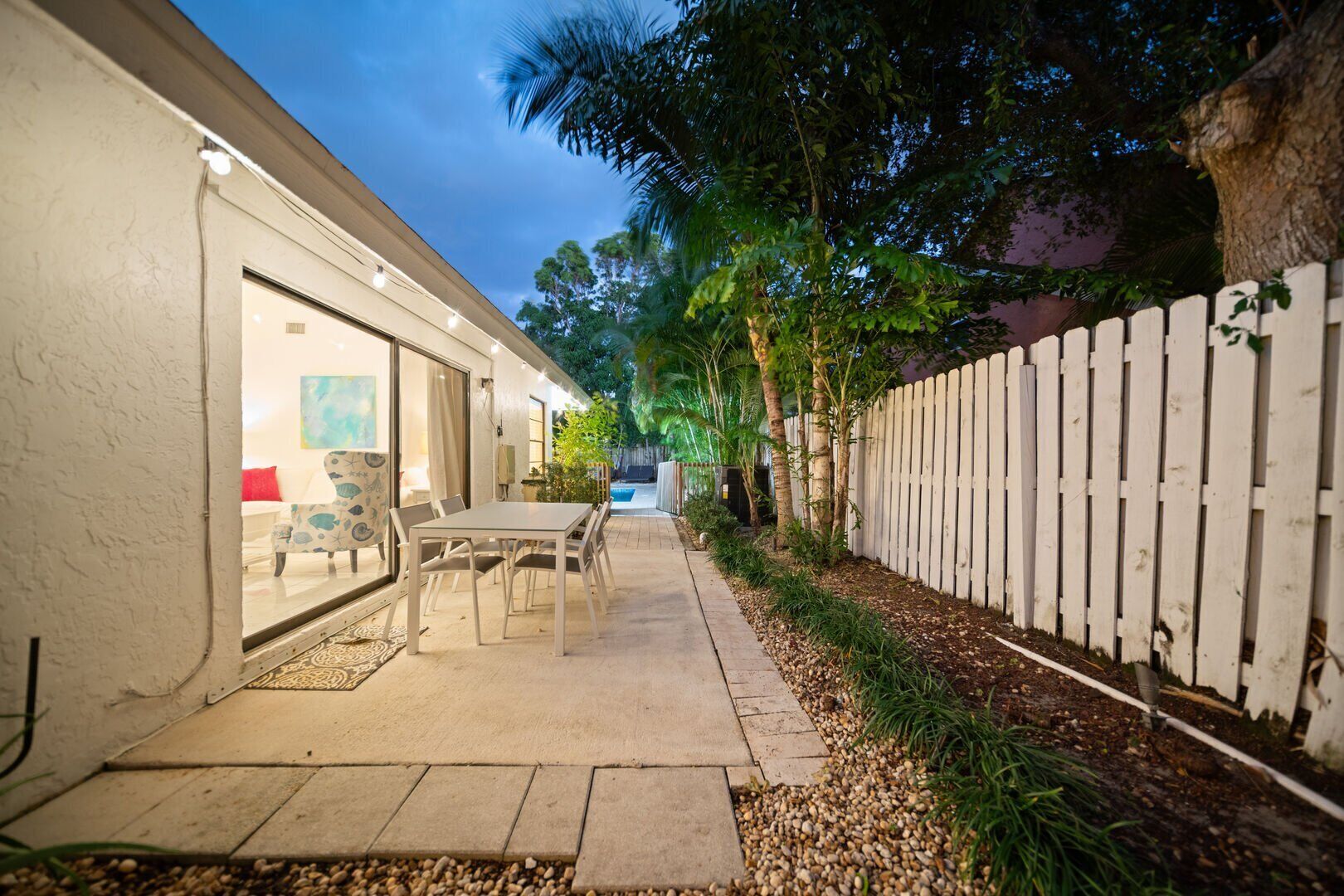 A patio area with a table and chairs, a white fence, and a view of a building with a glass door.