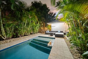 A swimming pool with a tiled deck, surrounded by lush greenery and a seating area with sofas and a table. - 2221 Managed by Brampton Park (Delray Beach)