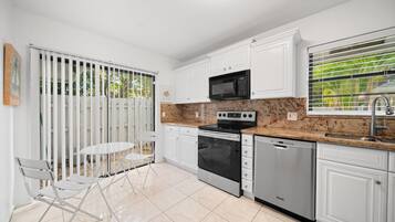 A modern kitchen with white cabinets, a granite countertop, a stove, a microwave, and a dishwasher.