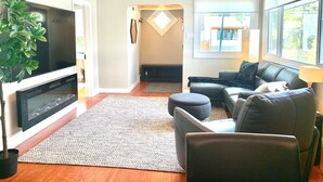 Ein Wohnzimmer mit Flachbildfernseher, grauem Sofa, Couchtisch und einer Topfpflanze.