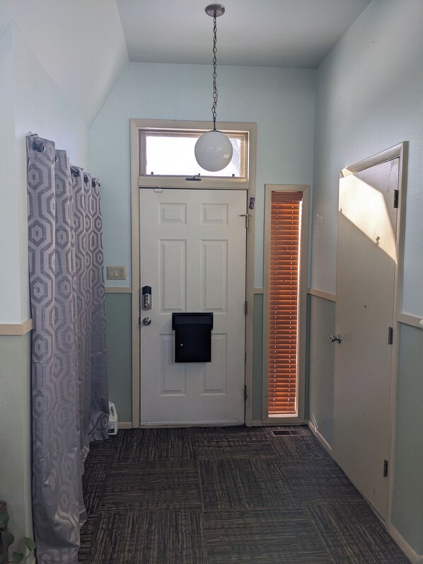 Un pasillo con una puerta, una ventana con persianas, un accesorio de iluminación y cortinas estampadas.