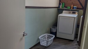 A laundry room with a washing machine, a drying machine, a basket, and a shelf with cleaning supplies.