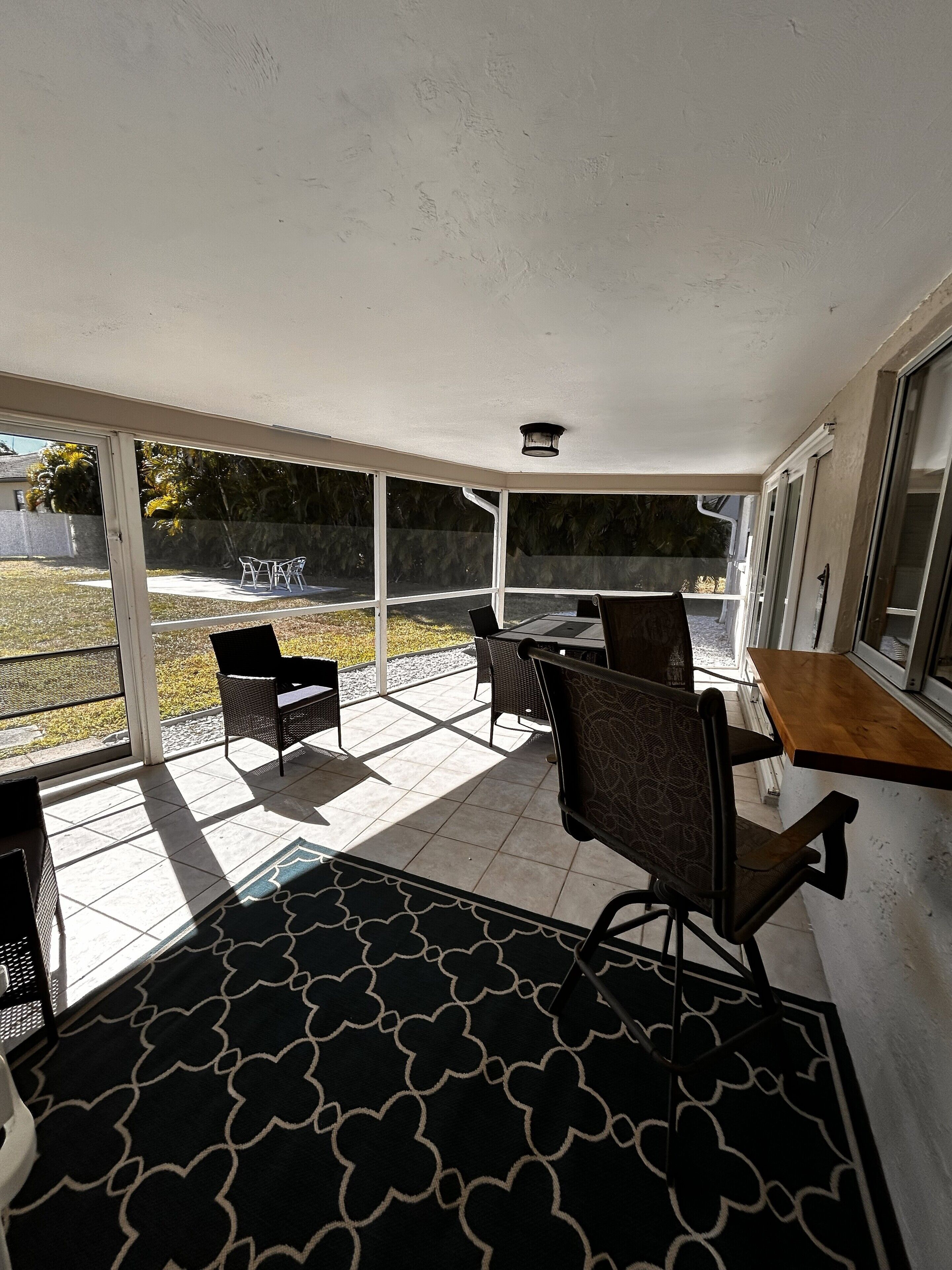 A covered patio area with a table and chairs, large windows, and a patterned rug.
