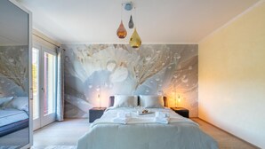 Un dormitorio con una cama grande, dos mesitas de noche, un mural en la pared y una puerta corredera de cristal que da a un balcón.