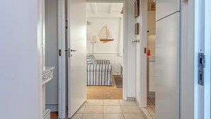 Un pasillo que conduce a un dormitorio con una cama a rayas, una decoración de velero colgado y un radiador.